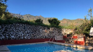 A swimming pool with a stone wall, a red border, and a view of mountains.