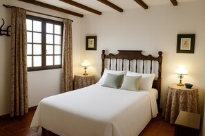 A bedroom with a large bed, two bedside tables with lamps, a window with curtains, and wooden beams on the ceiling.
