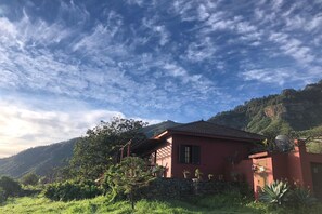 Une maison rouge avec un mur en pierre, entourée de verdure et de collines.