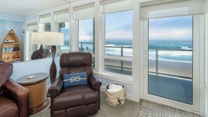 Una habitación con vista al océano, un sillón de cuero marrón, una mesita redonda pequeña, una lámpara y una estantería.