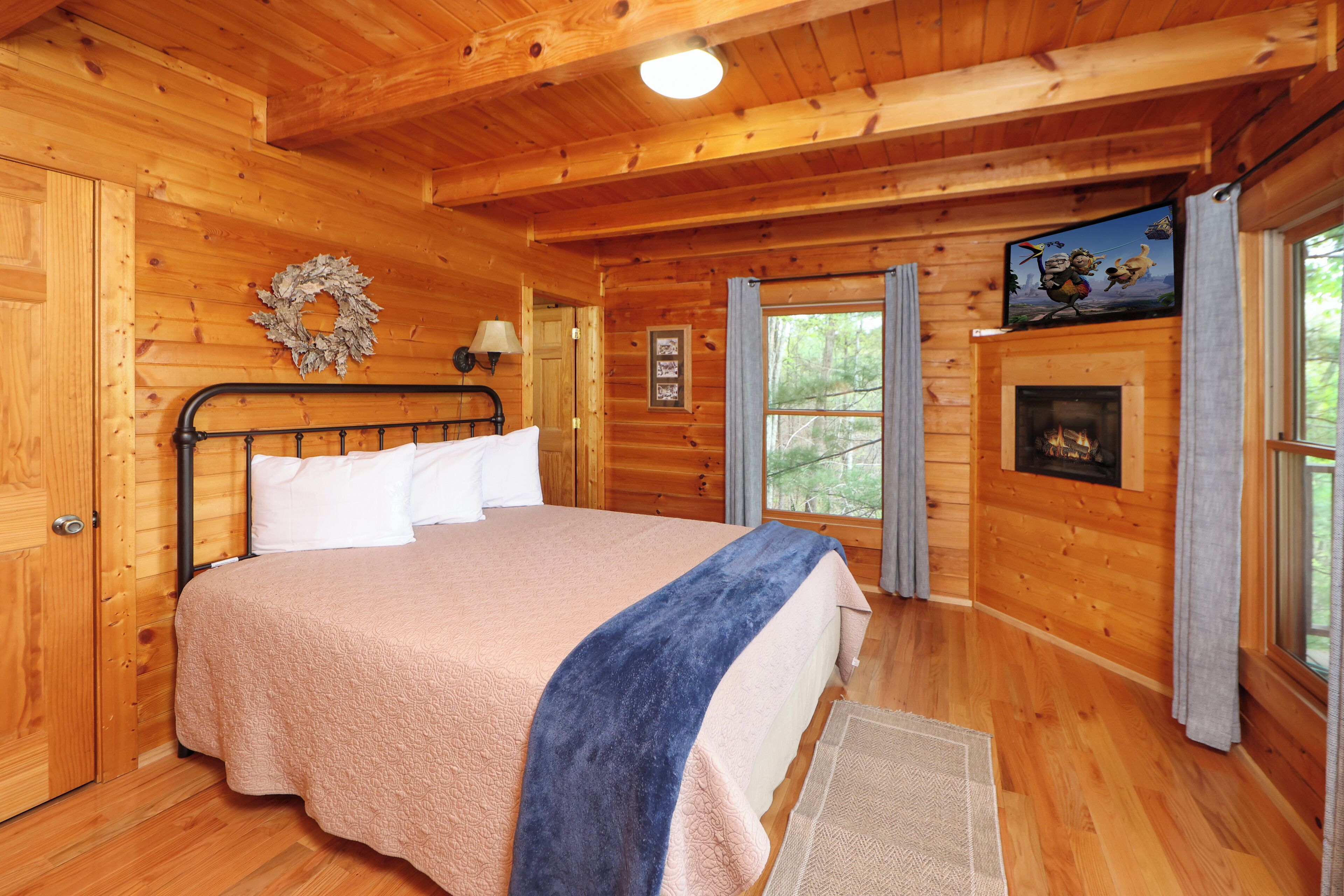 A wooden cabin bedroom with a bed, a fireplace, and a view of the outdoors.