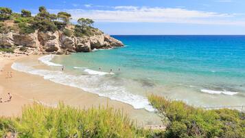 Una playa con aguas turquesas cristalinas, acantilados rocosos y vegetación verde.