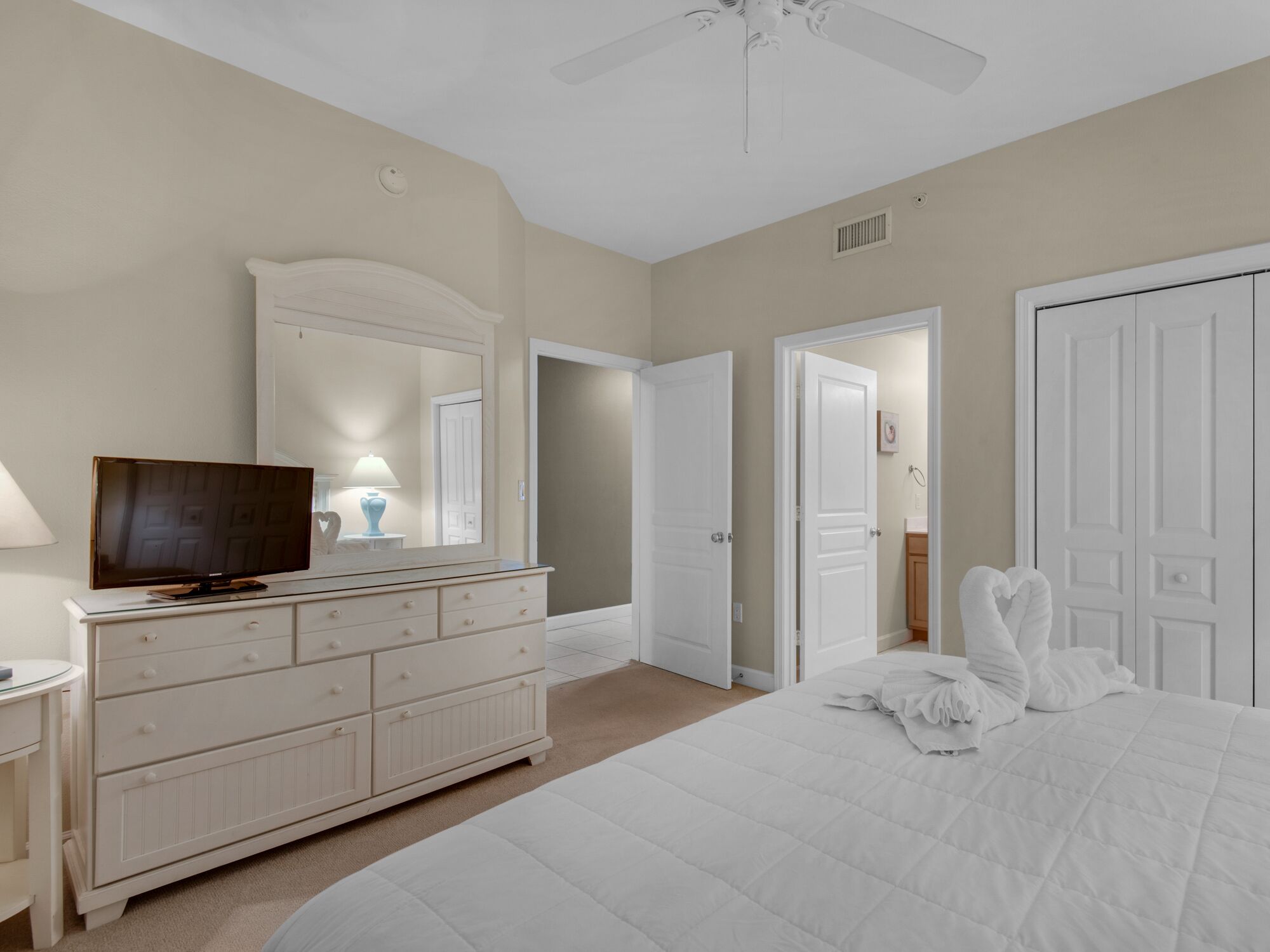 A bedroom with a bed, a dresser, a television, and a ceiling fan.