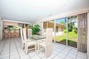 A modern kitchen with white cabinets, a dining area with a glass table and white chairs, and a large sliding glass door leading to a garden. - SWISS 41 - Golf Course (Clermont)