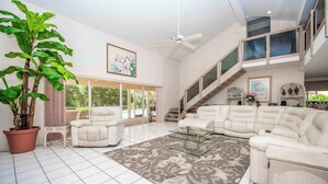 A spacious living room with a large potted plant, a glass coffee table, a beige sectional sofa, and a staircase leading to an upper level. - SWISS 41 - Golf Course (Clermont)