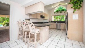 A modern kitchen with a central island, bar stools, and a view of greenery outside. - SWISS 41 - Golf Course (Clermont)
