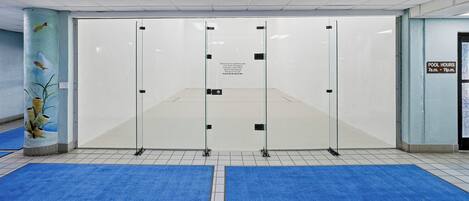 Une pièce dotée d’une grande paroi en verre, de tapis bleus sur le sol et d’un panneau indiquant les heures d’ouverture de la piscine.