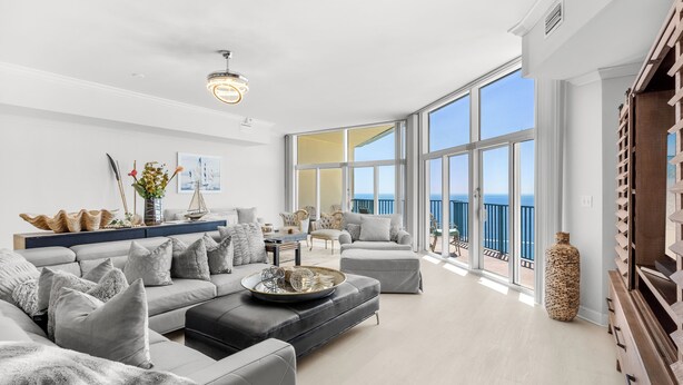 Un salon spacieux, doté d’un grand canapé, d’une table basse et offrant une vue sur la mer grâce à de grandes fenêtres.