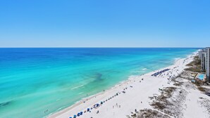 Une plage à l’eau turquoise et limpide, au sable blanc, bordée d’une rangée de parasols bleus.