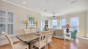 A spacious room with a wooden dining table, white upholstered chairs, a blue sofa, and a view of the ocean through large windows.