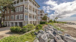 A multi-story beachfront hotel with balconies, a stone facade, and a view of the beach.