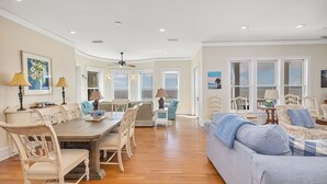 A spacious living area with a wooden dining table, multiple chairs, a sofa, and a view of the ocean through large windows.