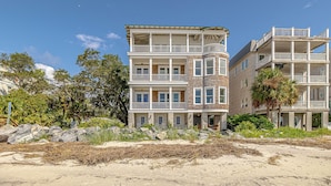 A multi-story beachfront hotel with balconies, a sandy beach in front, and surrounding vegetation.