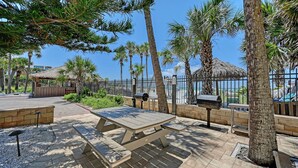 A patio area with a picnic table, a barbecue grill, and a thatched-roof structure. - Siesta Key Beachfront Vacation Condo - great value and many amenities! (Sarasota)