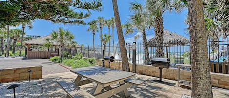 A patio area with a picnic table, a barbecue grill, and a thatched-roof structure.