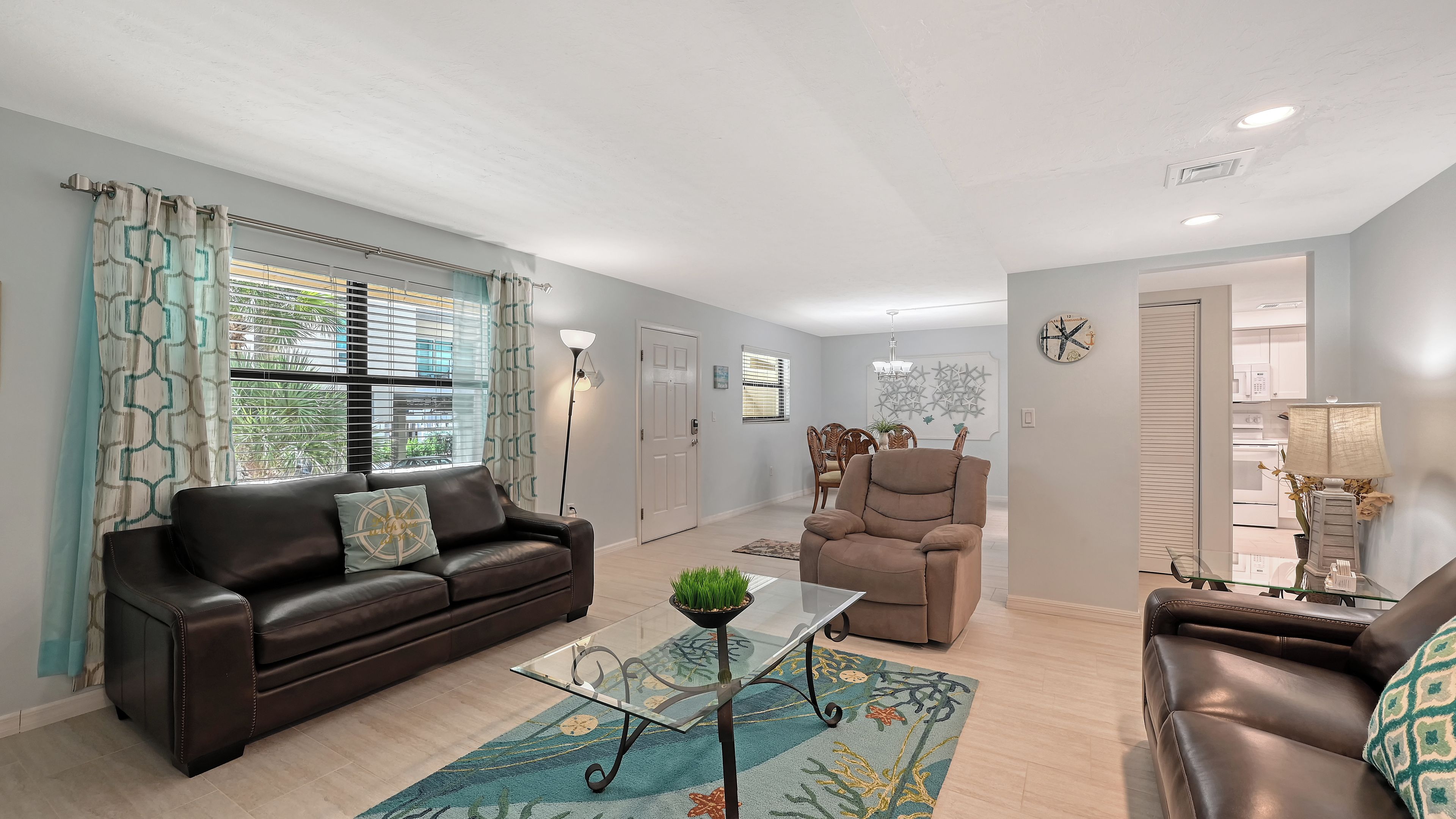 A modern living room with a brown leather sofa, a glass coffee table, and a beige armchair.