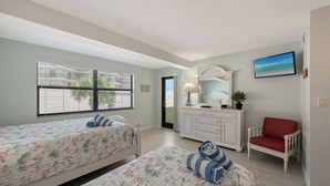 A bedroom with two beds, a dresser, a chair, and a TV. - Siesta Key Beachfront Vacation Condo - great value and many amenities! (Sarasota)