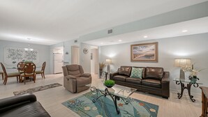 A modern living room with a glass coffee table, leather sofa, and dining area with wooden chairs. - Siesta Key Beachfront Vacation Condo - great value and many amenities! (Sarasota)