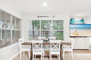 A dining area with a table and chairs, a view of the outdoors, and a decorative wall piece.