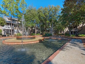 A courtyard with a central fountain, surrounded by trees and a building with a balcony.