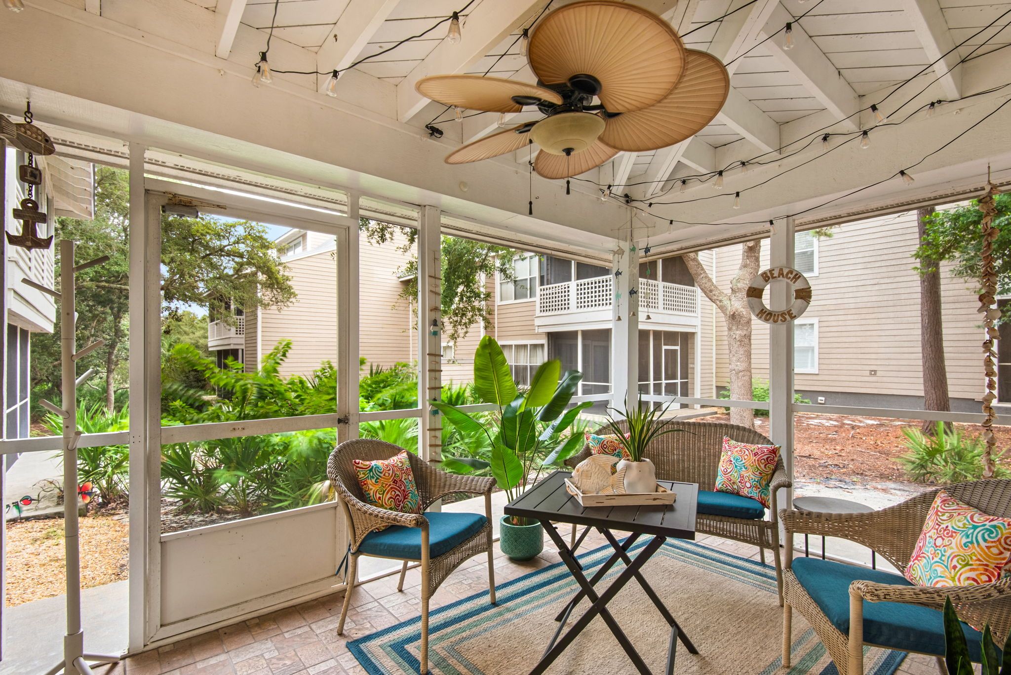 A sunroom with wicker furniture, a ceiling fan, and large windows overlooking a garden.
