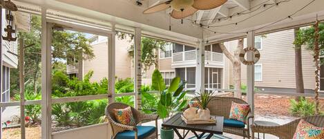 A sunroom with wicker furniture, a ceiling fan, and large windows overlooking a garden.