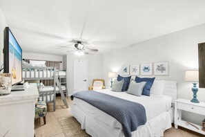 A bedroom with a bed, bedside tables, a desk, a chair, a ceiling fan, and framed pictures on the wall.