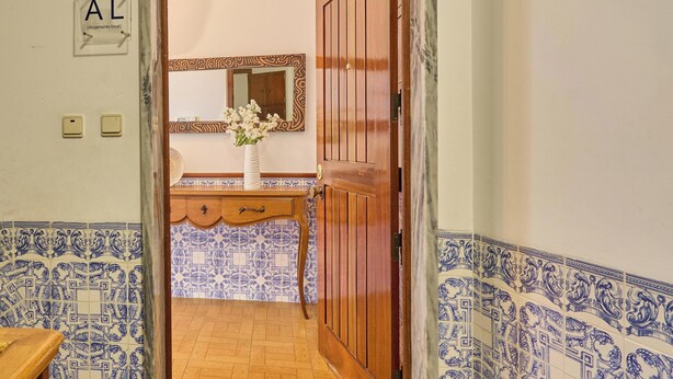 A hallway with blue and white patterned tiles, a wooden door, and a sign indicating a 'Clean & Safe' establishment. - Palace View Apartment- Downtown Mafra (Mafra)