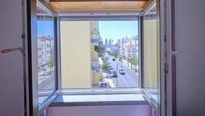 A view from a window with a wooden ceiling, looking out onto a street with buildings and parked cars. - Palace View Apartment- Downtown Mafra (Mafra)