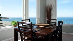 Un coin repas avec vue sur l’océan, comprenant une table en bois, des chaises et un luminaire suspendu.