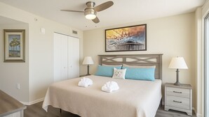 Une chambre d’hôtel avec un lit, deux tables de chevet, un ventilateur de plafond, un tableau et une fenêtre.
