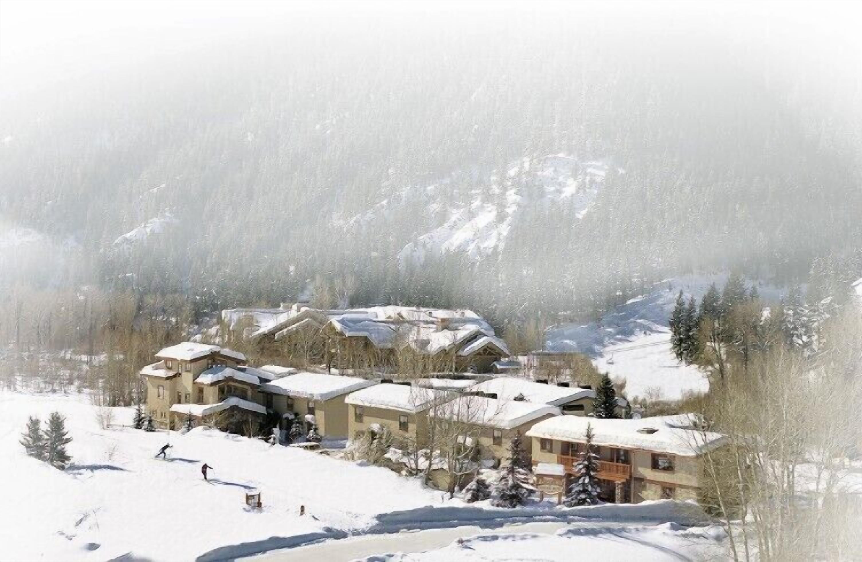 A snow-covered resort with multiple buildings, ski slopes, and a mountainous backdrop.