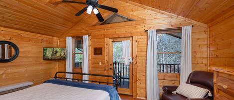 A wooden cabin room with a bed, a leather chair, a ceiling fan, and a balcony door.
