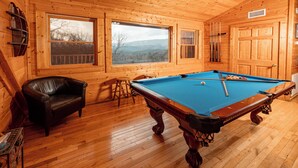 A wooden interior with a pool table, a leather chair, and large windows. - Beautiful Mountain View Overlooking The Smokies! Hot Tub, Pool Table, Mini Golf (Sevierville)