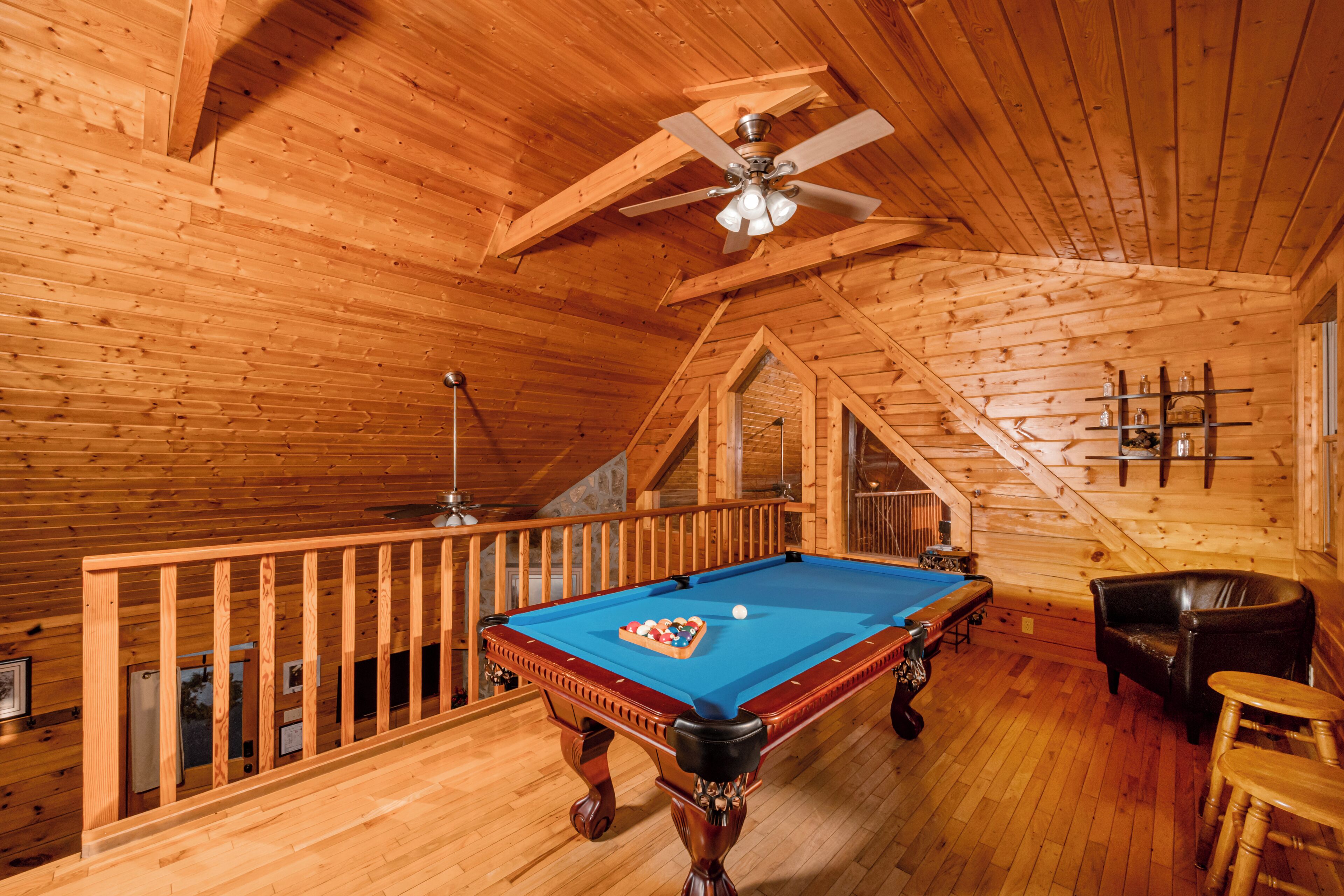 A wooden interior with a pool table, a ceiling fan, and a leather chair.