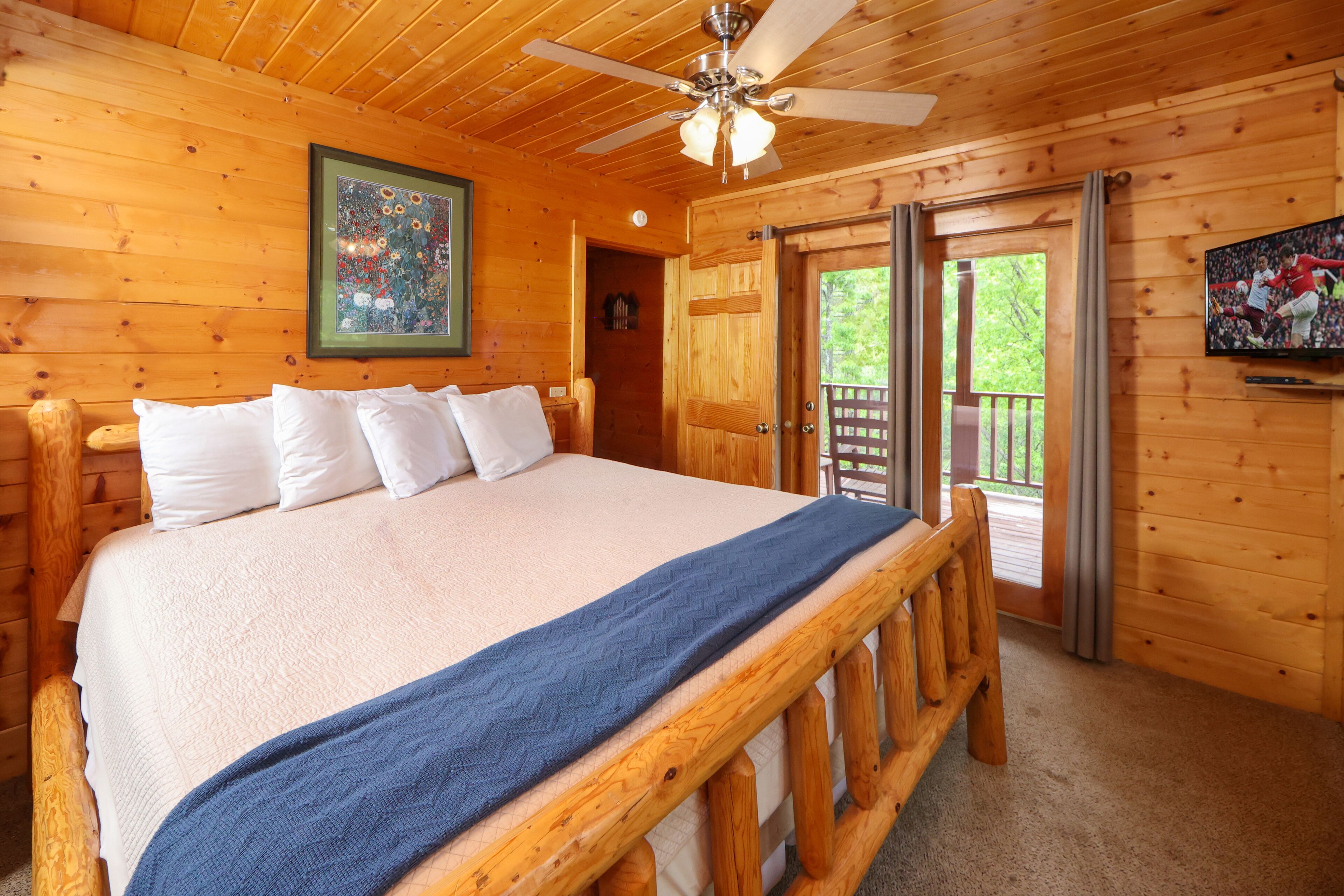 Une chambre située dans une cabane en bois, avec un lit, un ventilateur de plafond et une porte donnant sur une terrasse extérieure.