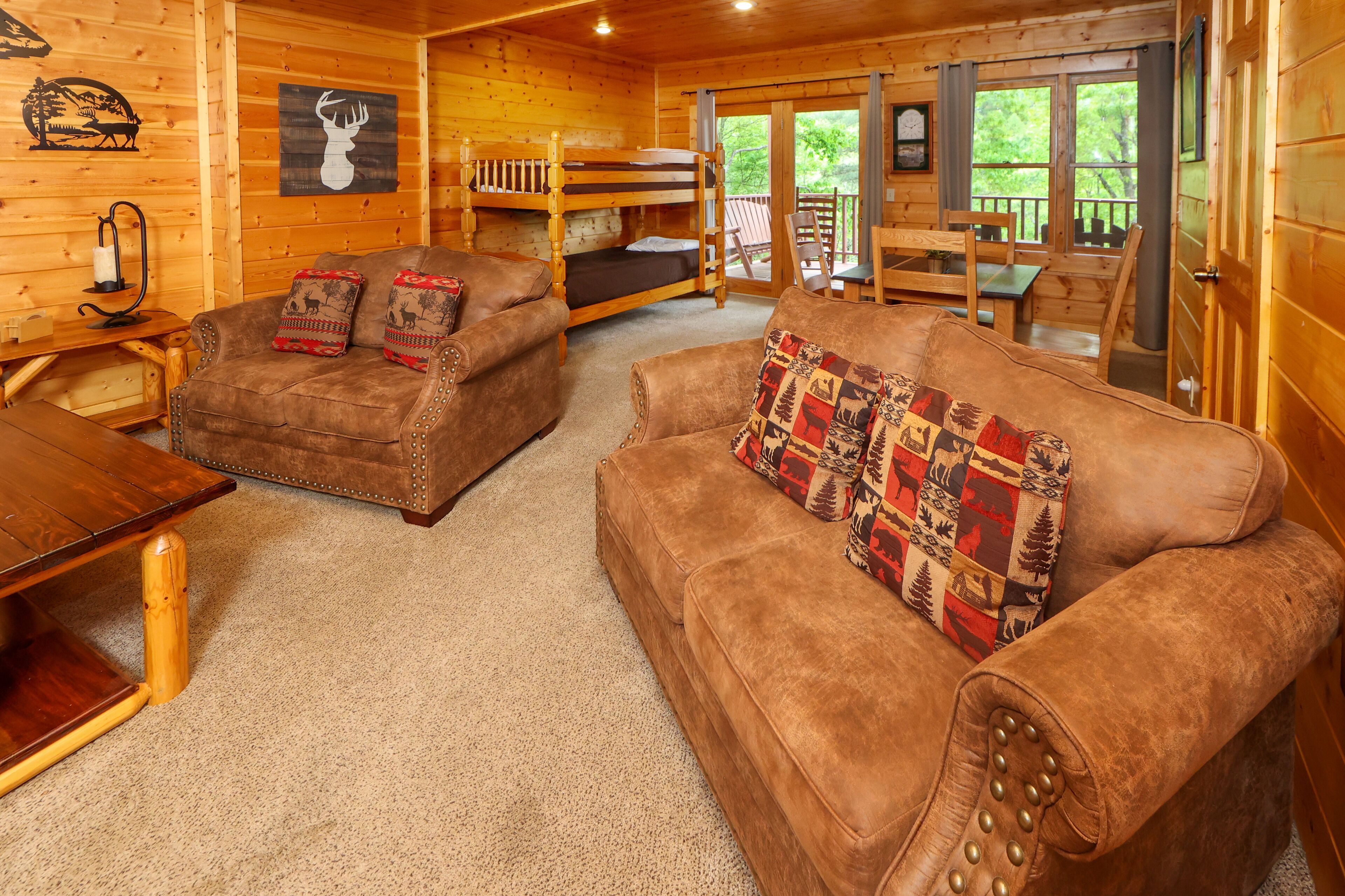 A cozy cabin interior with a wooden interior, a bunk bed, a brown leather sofa, and a dining table.