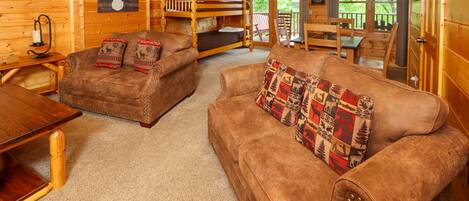 A cozy cabin interior with a wooden interior, a bunk bed, a brown leather sofa, and a dining table.