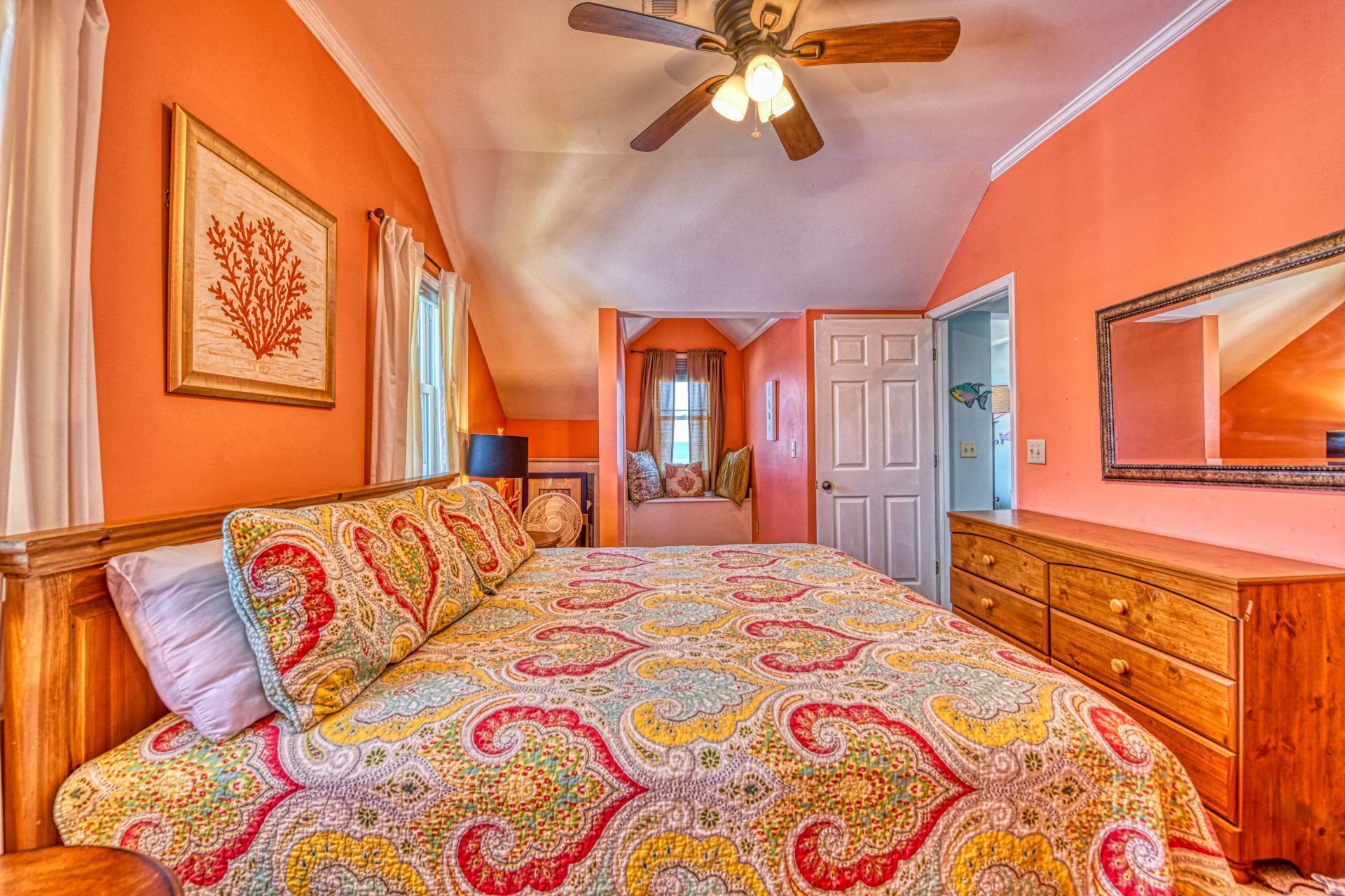 A bedroom with a large bed, a ceiling fan, a dresser, and a window with curtains.