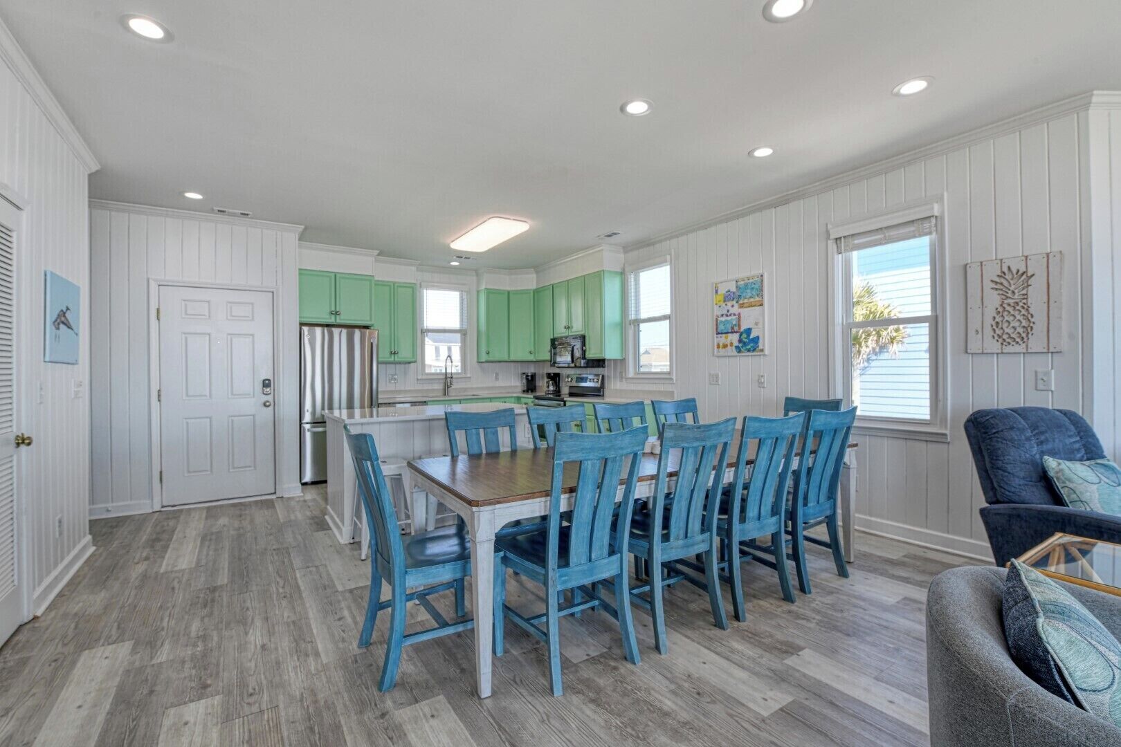 A spacious kitchen with green cabinets, a dining area with blue chairs, and a gray sofa.