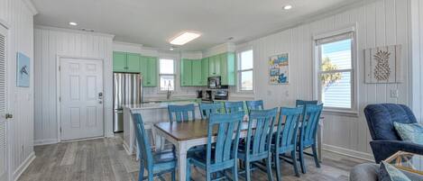 A spacious kitchen with green cabinets, a dining area with blue chairs, and a gray sofa.
