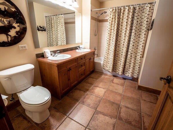 Et badeværelse med toilet, håndvask, underskab og bruser.