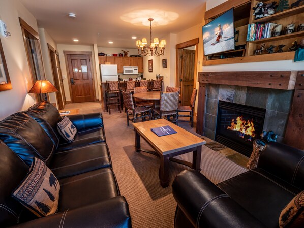 A living room with a fireplace, leather sofa, dining area, and kitchen in the background.