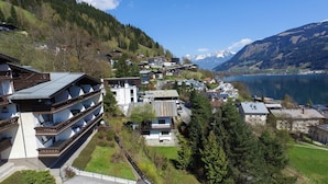 A hillside residential area with modern and traditional buildings, a parking lot, and a lake with mountains in the background. - Apartment THE GOOD VIEW I - Lake & Mountain view (Zell am See)