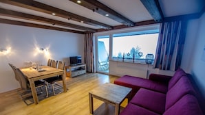 A modern living room with a wooden dining table, purple sofa, and a TV on a stand. - Apartment THE GOOD VIEW I - Lake & Mountain view (Zell am See)