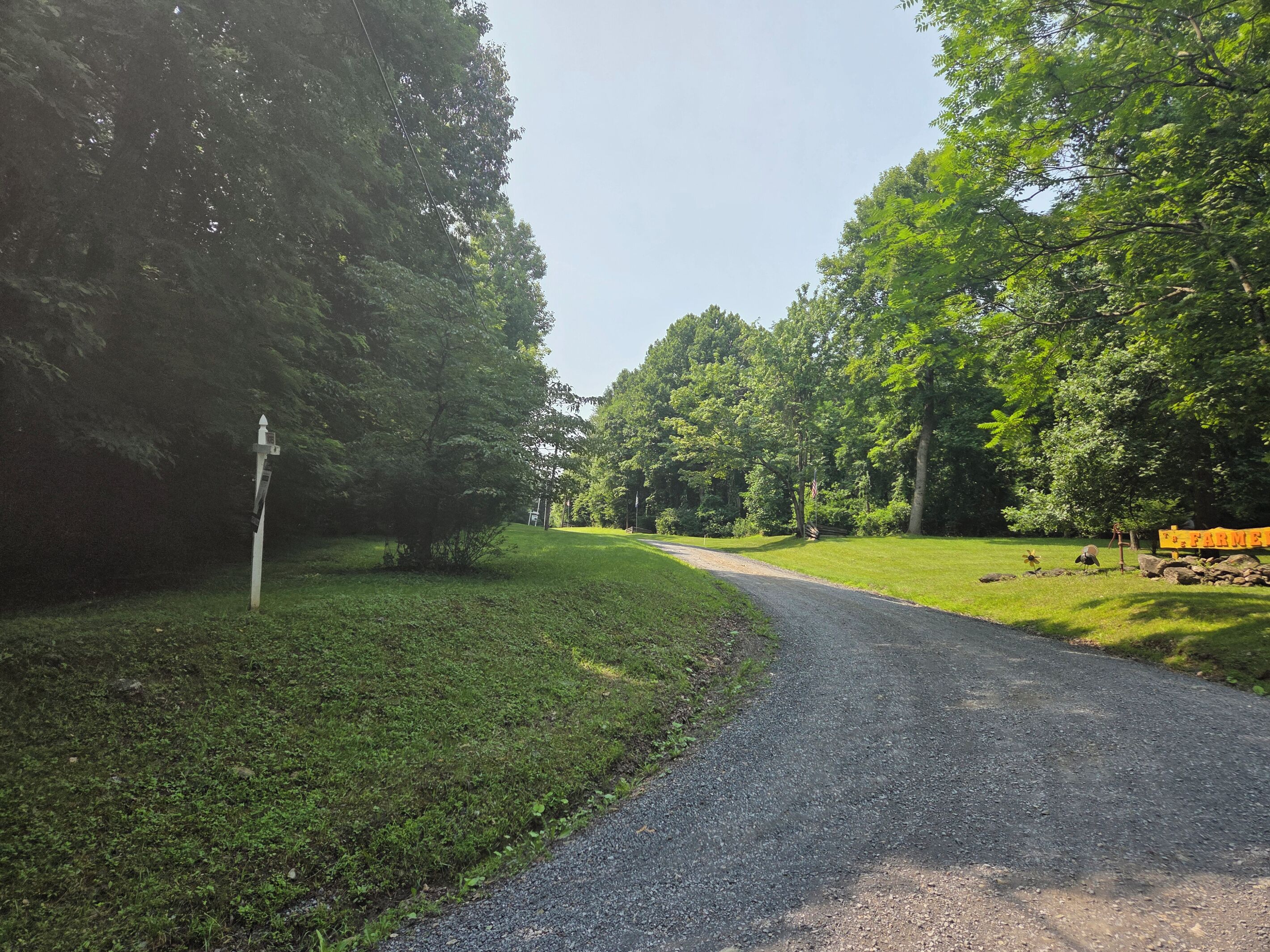 A gravel path leading through a park with trees and a wooden sign.