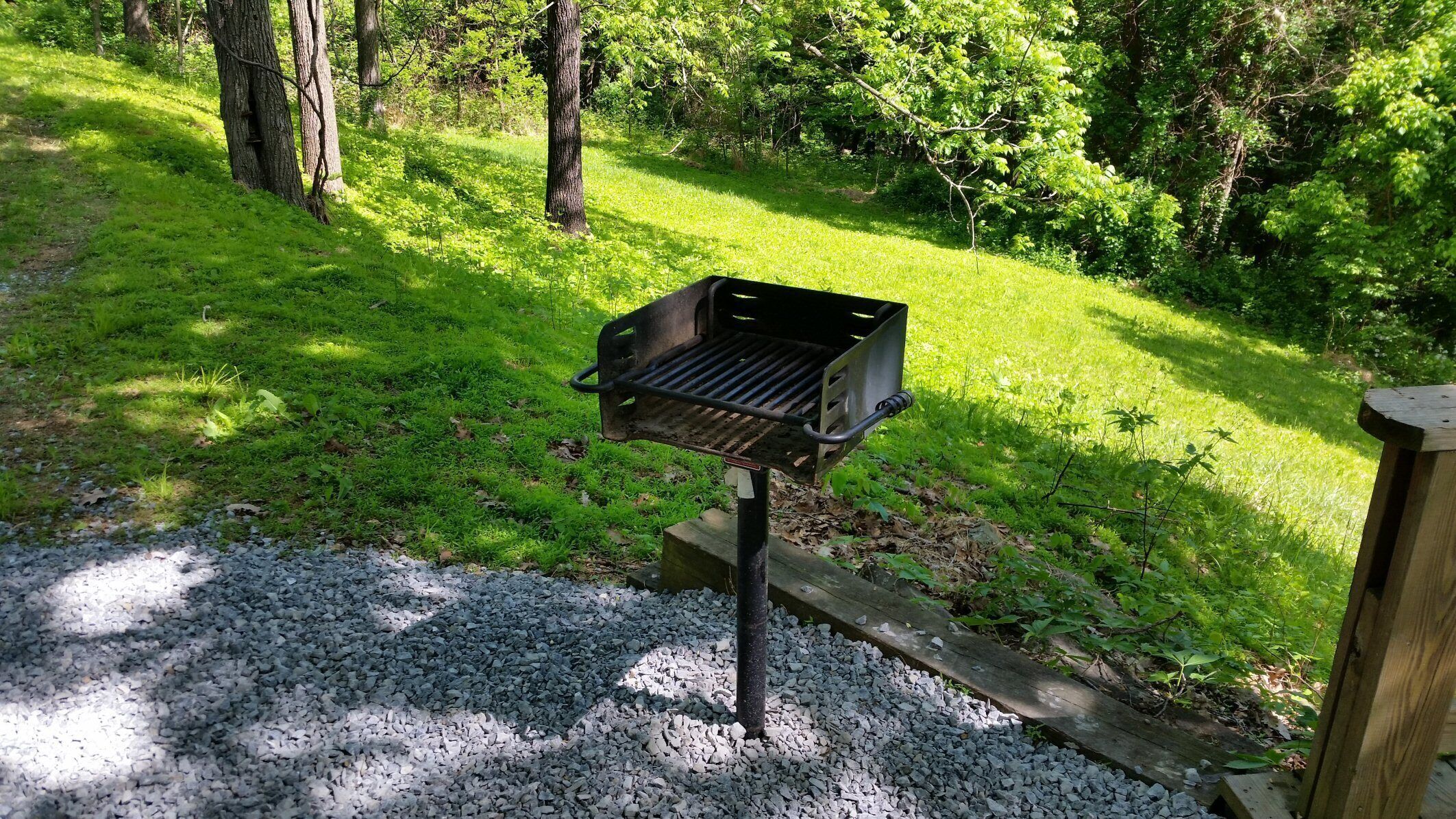 A portable grill in a grassy area with trees in the background.