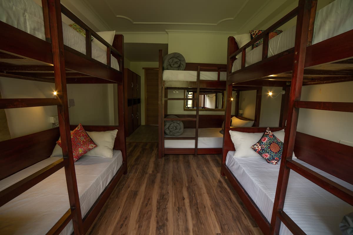 Quarto com beliches, piso de madeira e janela com cortinas.