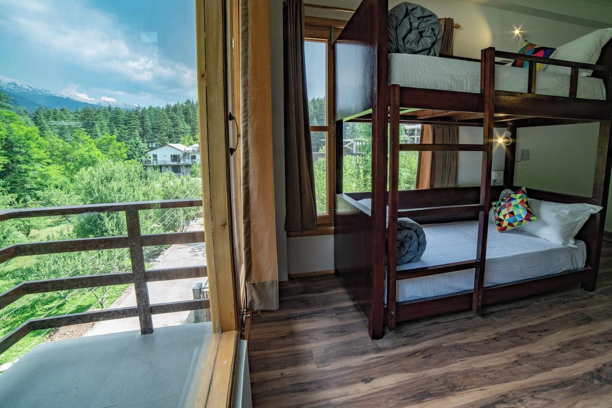 Quarto com beliche e vista para uma floresta e casas.