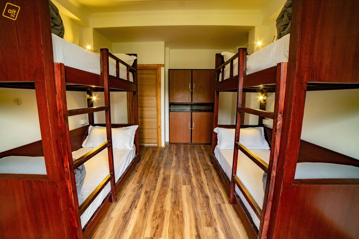 Quarto com beliches de madeira e roupa de cama branca.